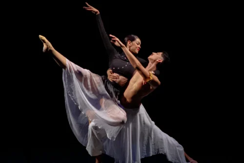 Dva tanečníci předvádějí paso doble na černém pozadí. Žena má na sobě černý top a splývavou bílou sukni. Má zvednutou nohu a nataženou ruku. Muž je bez trička a má na sobě splývavou bílou sukni. Podpírá ženu a dívá se na ni. Oba vypadají soustředěně a vášnivě.